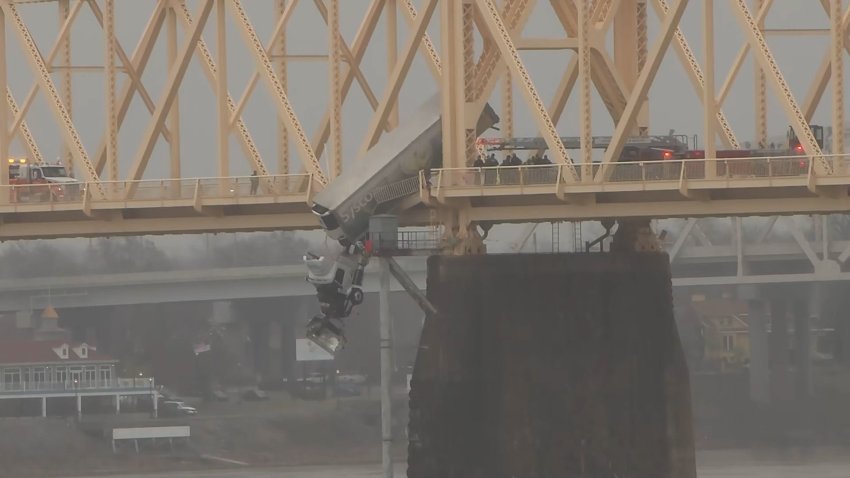 A semi-truck dangles off a bridge